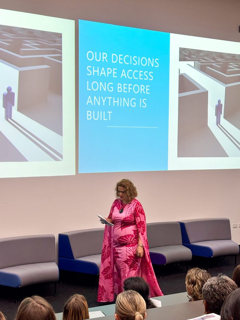 Presenter standing in front of a projector screen during an AWEC Symposium session