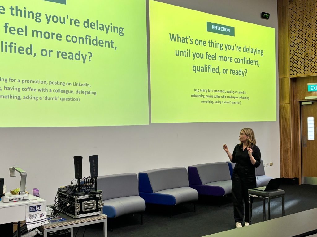 Presenter standing in front of a projector screen during an AWEC Symposium session